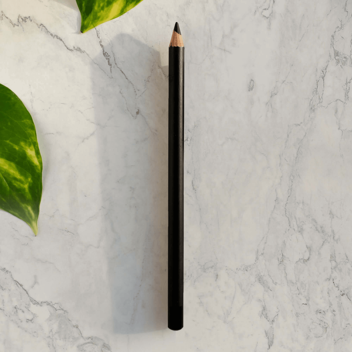 Black eyeliner pencil on marble surface with green leaves; premium MIANIMED skincare product.