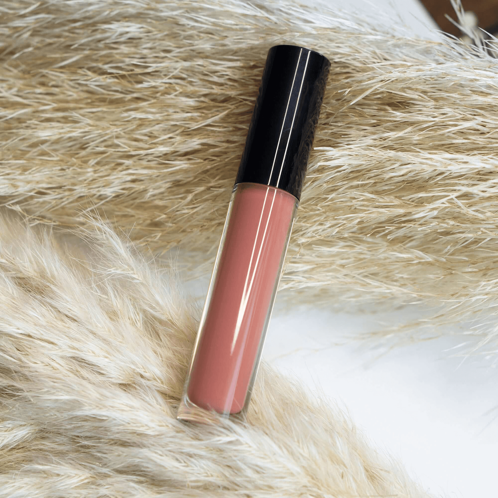 Premium MIANIMED skincare lip gloss in a sleek package, nestled on soft, beige pampas grass backgrounds.