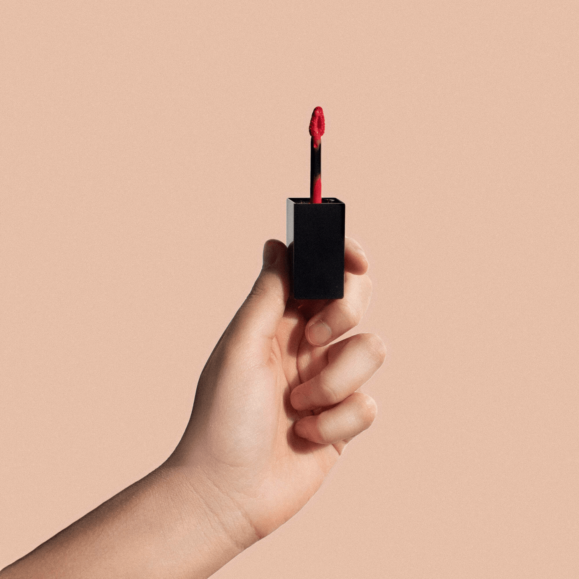 Hand holding luxurious red liquid lipstick in a sleek black tube, showcasing premium MIANIMED skincare and beauty products.